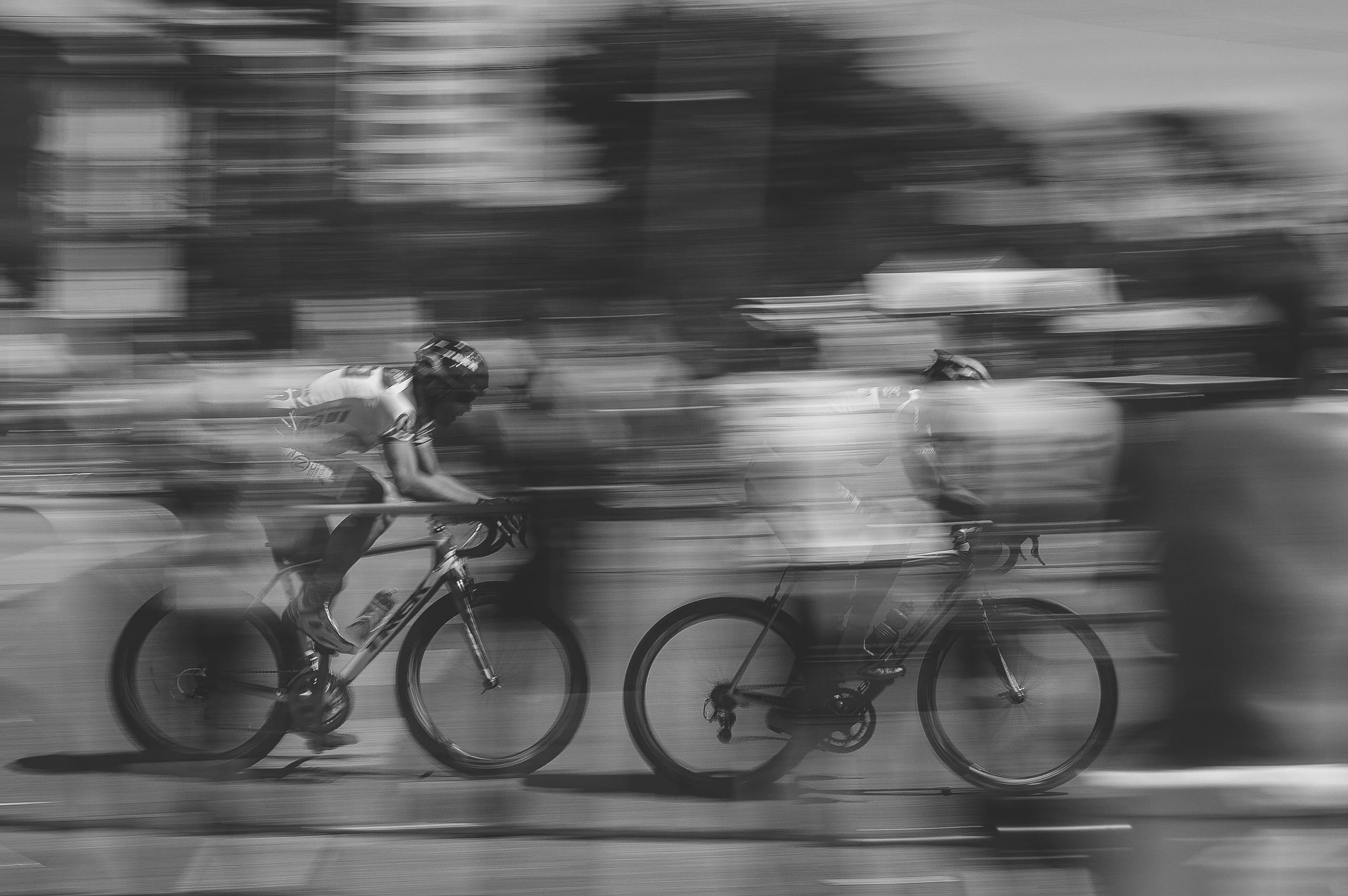 Cyclists racing through a blurred black-and-white street scene.